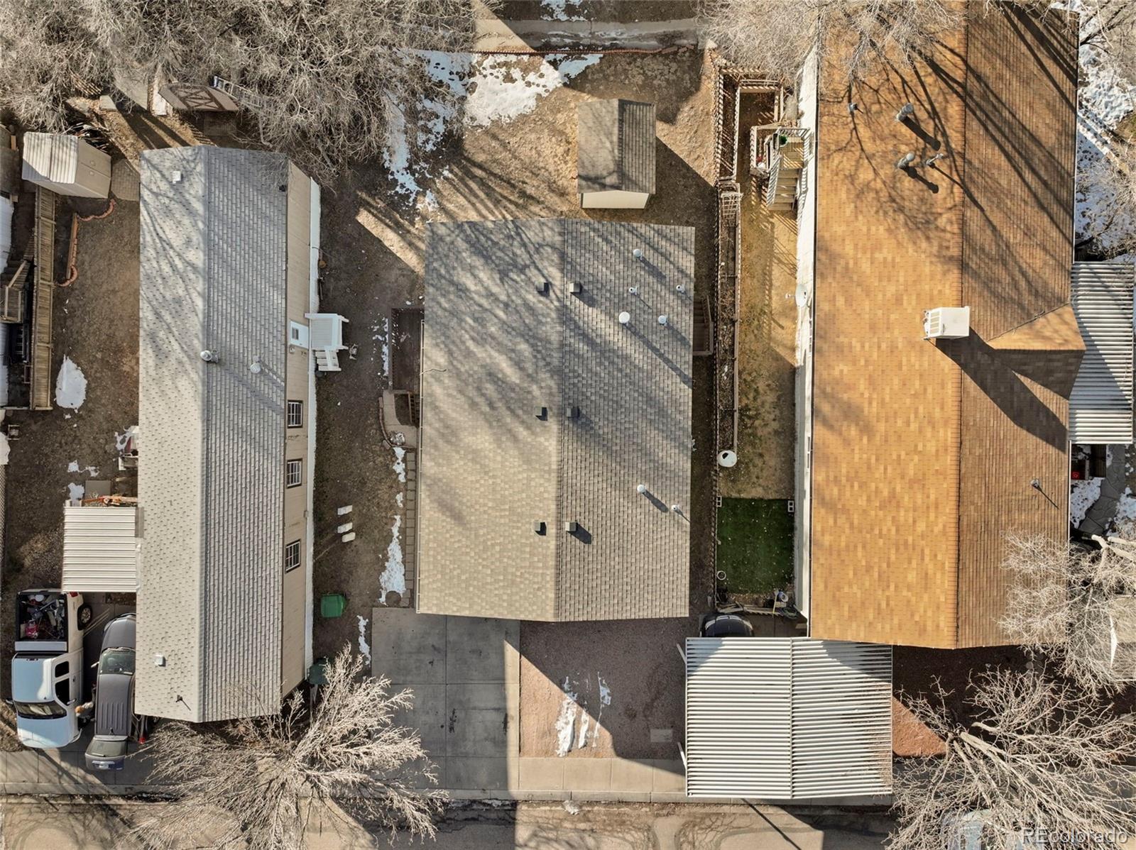 Aerial view of a gray-roofed home, driveway, and small yard with patches of snow.