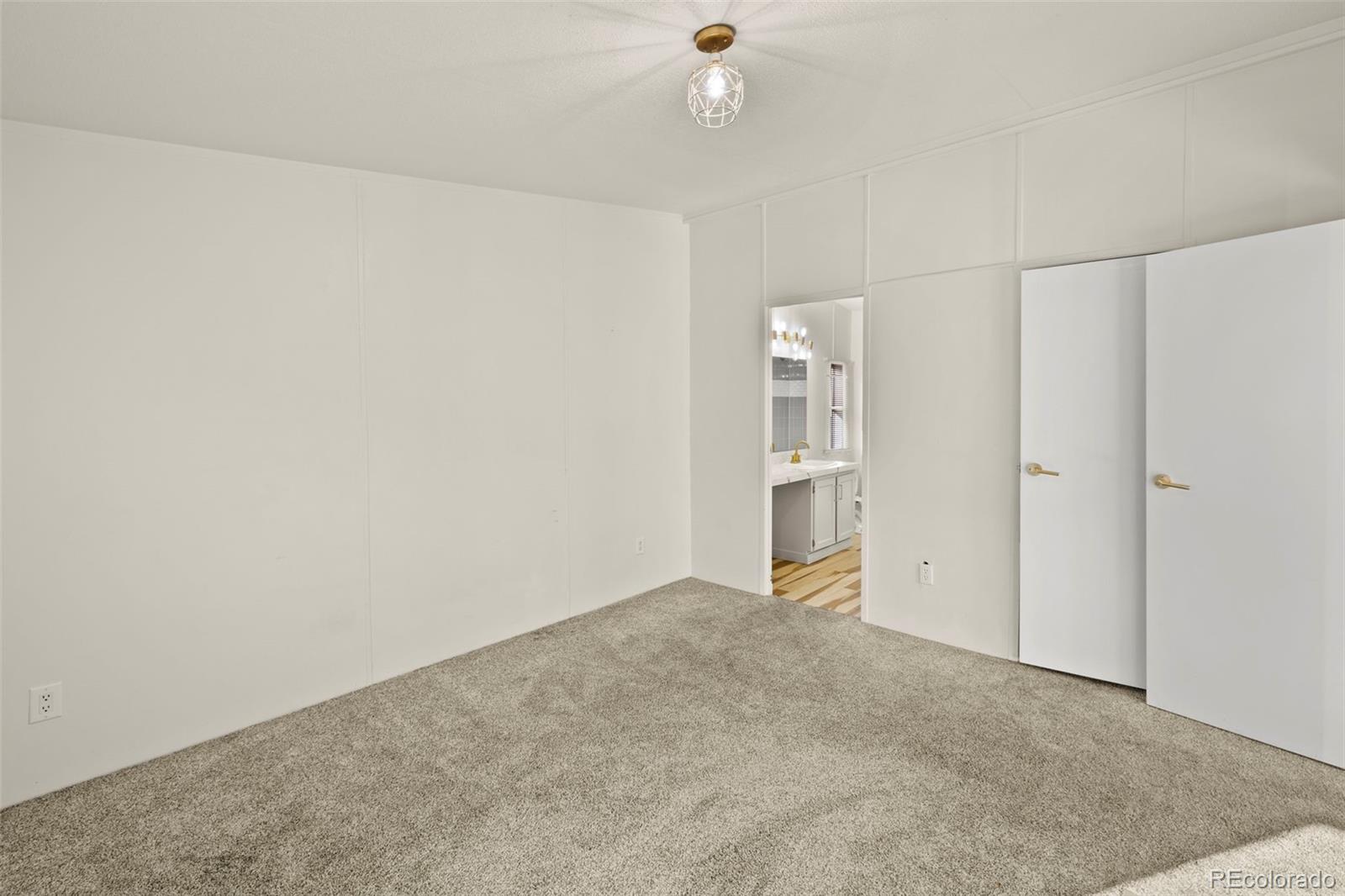 Empty carpeted bedroom with white double doors and an open doorway to a bathroom.