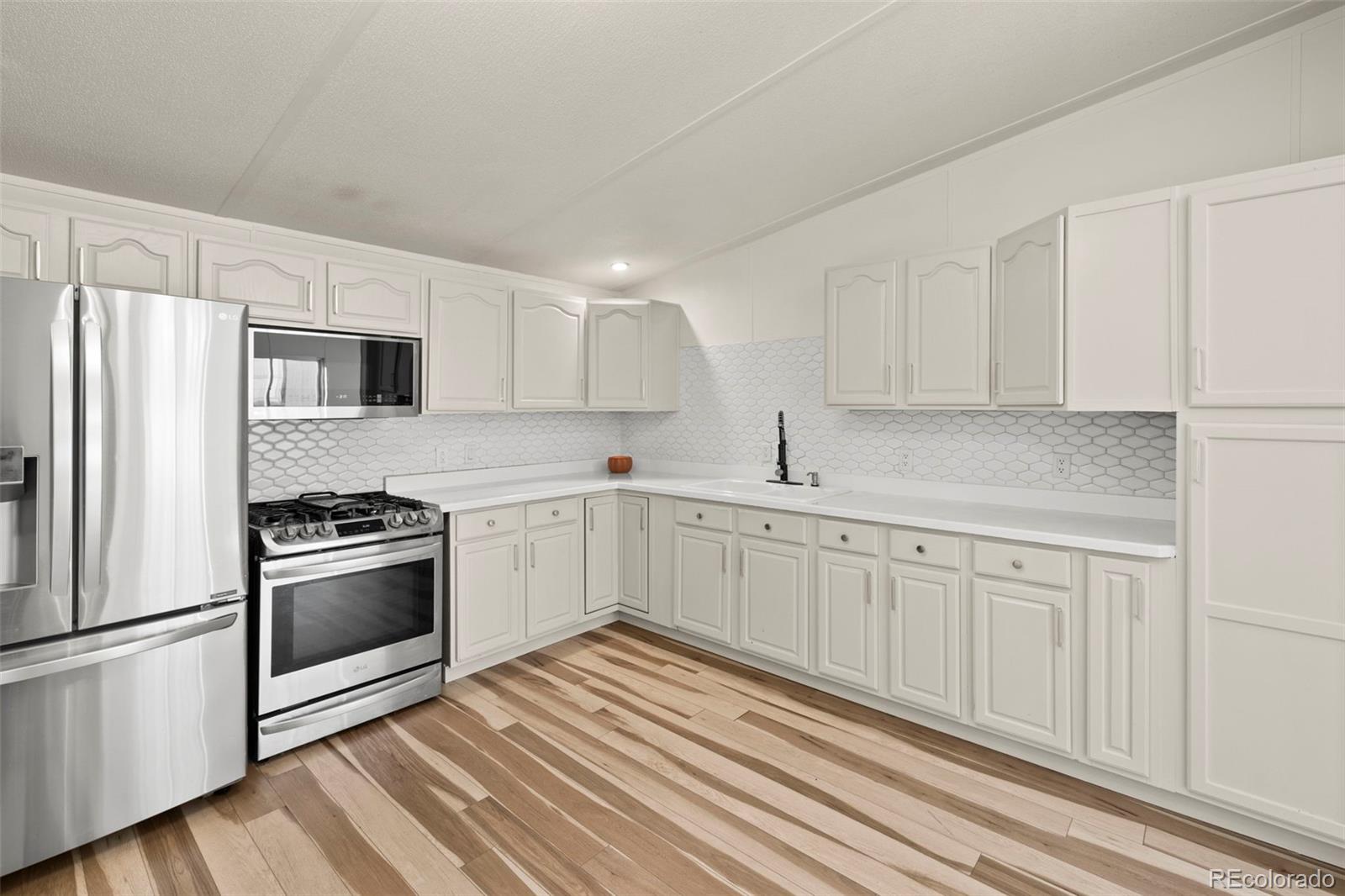 Kitchen with white cabinets, stainless appliances, hexagonal tile backsplash, and multitone wood flooring.
