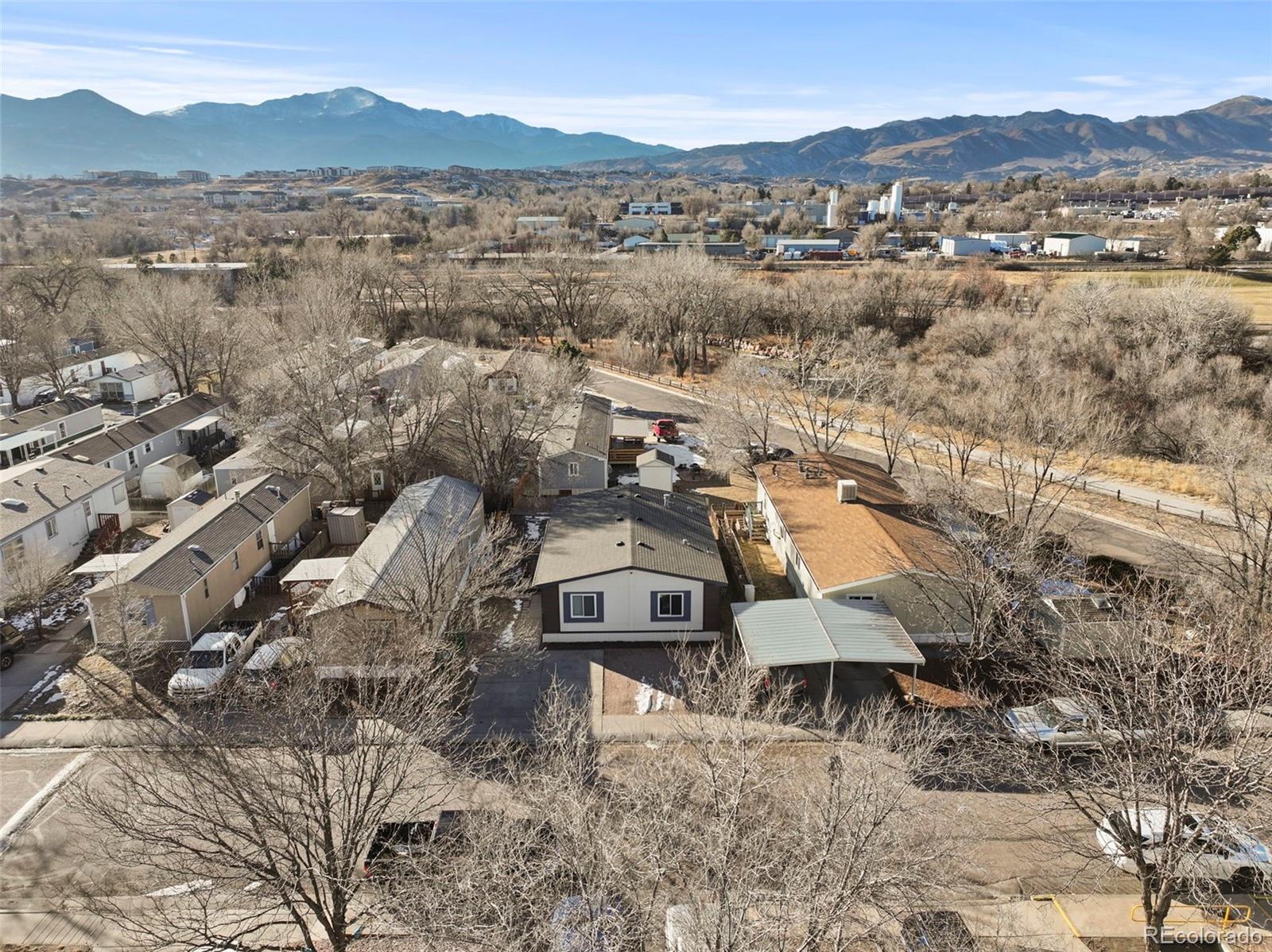 Aerial view of a home among leafless trees, with the Rocky Mountains beyond the neighborhood.