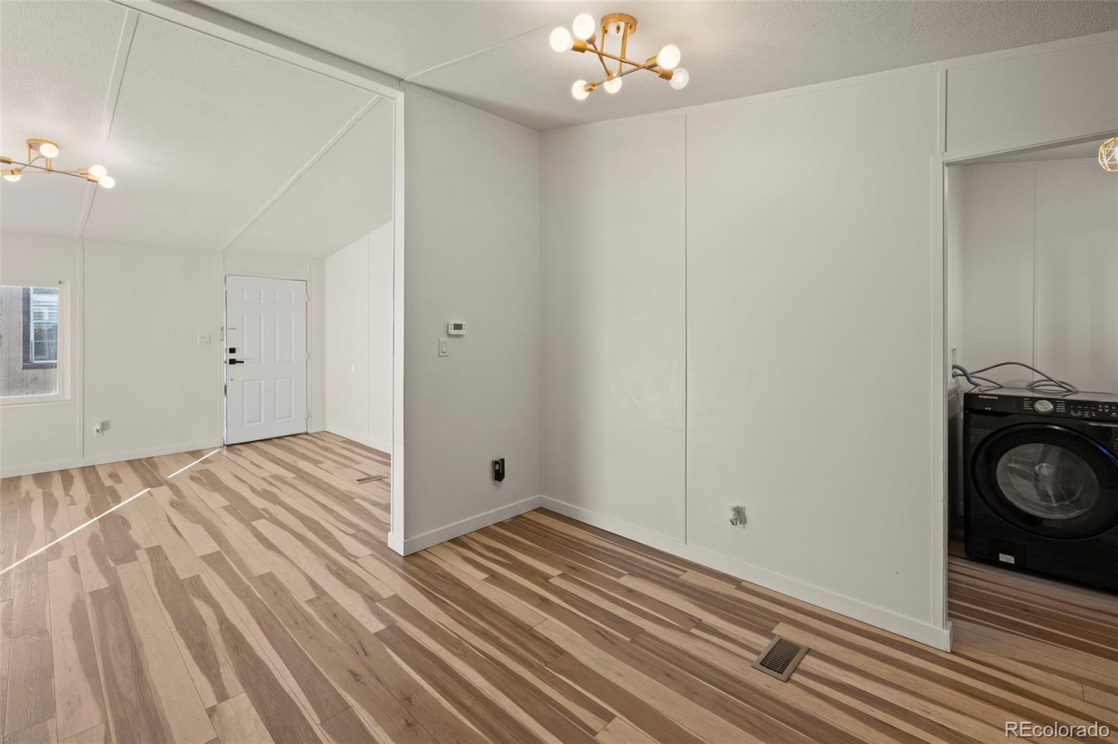 Empty room with striped wood-look floors, brass ceiling lights, and a washer in the adjoining laundry area.