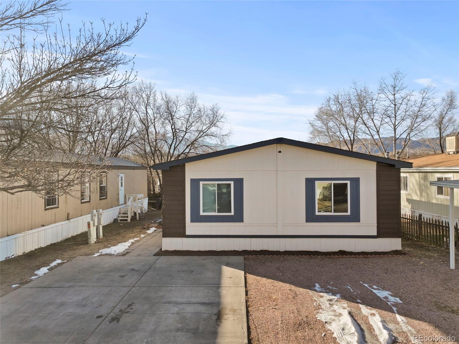 Single-story home with dark blue window trim, a concrete driveway, and snow patches in the yard.
