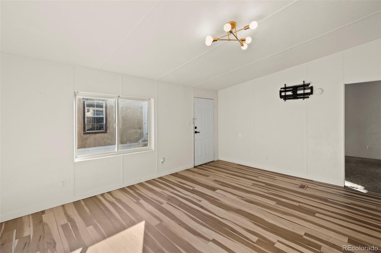 Empty living room with patterned wood-look flooring, a large window and a modern ceiling light.
