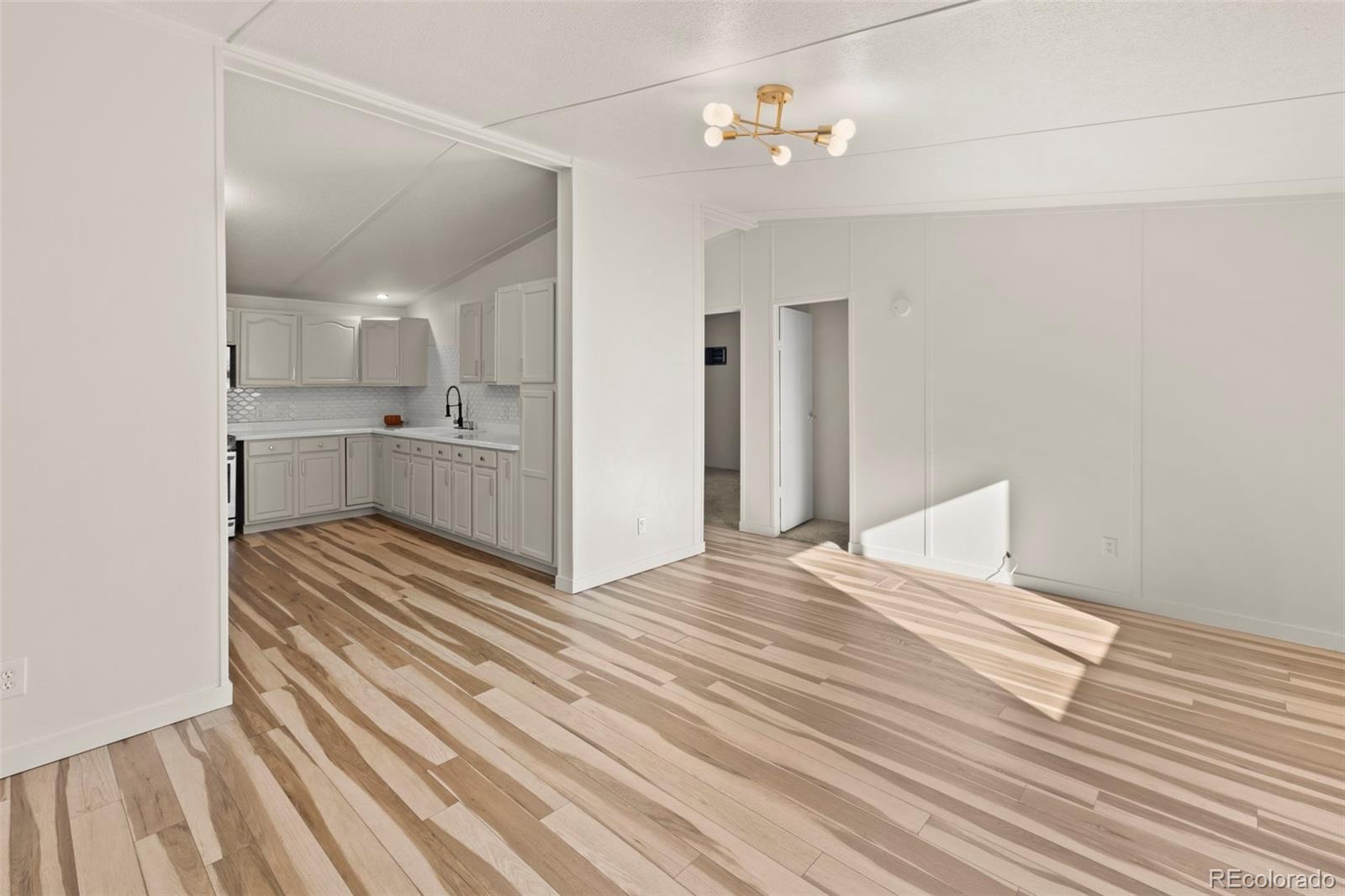 Open kitchen and adjoining room with white cabinets and distinctive multitone wood flooring.
