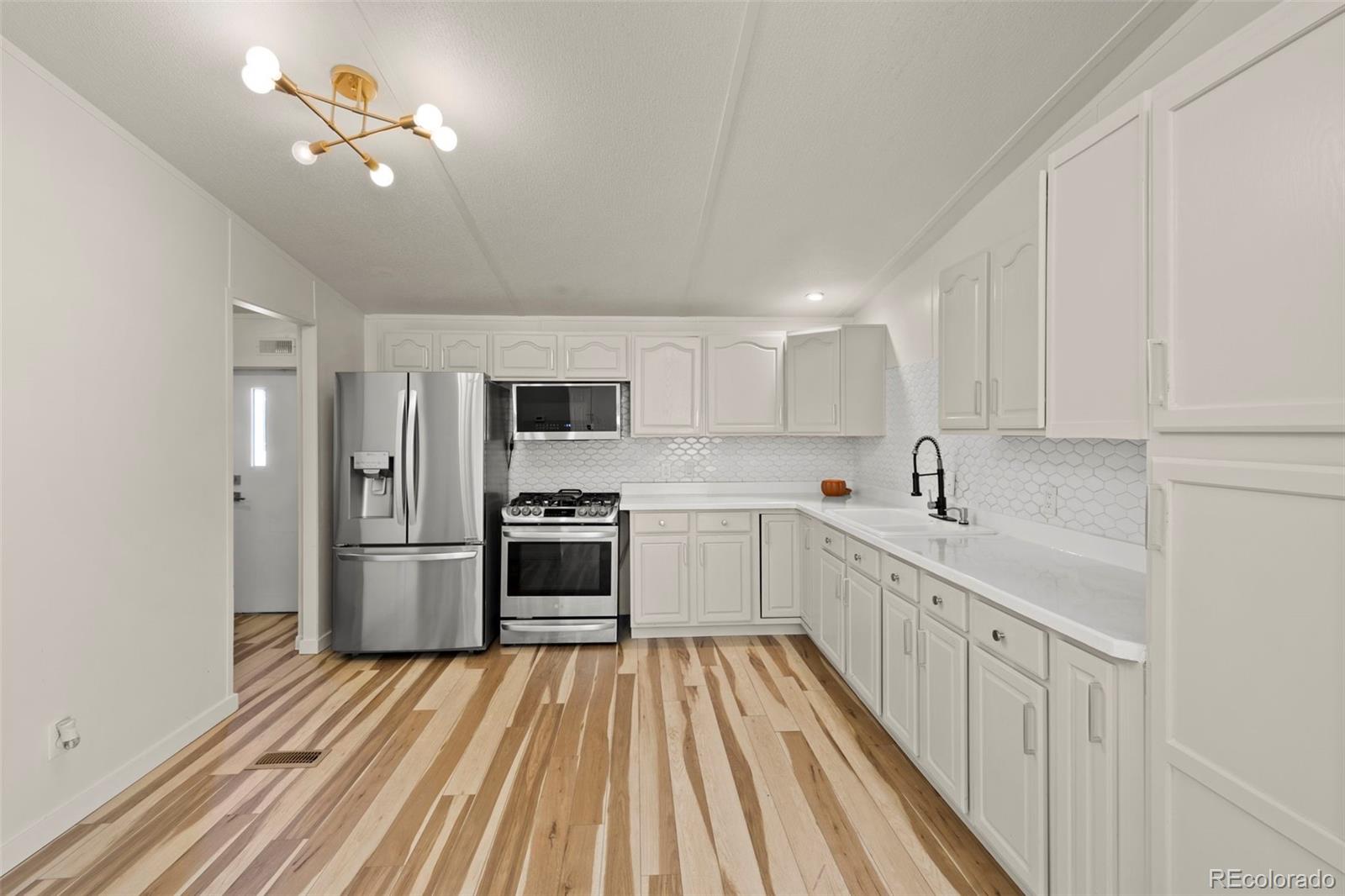 Kitchen with white cabinets, stainless appliances, hex tile backsplash, and multicolored wood plank flooring.