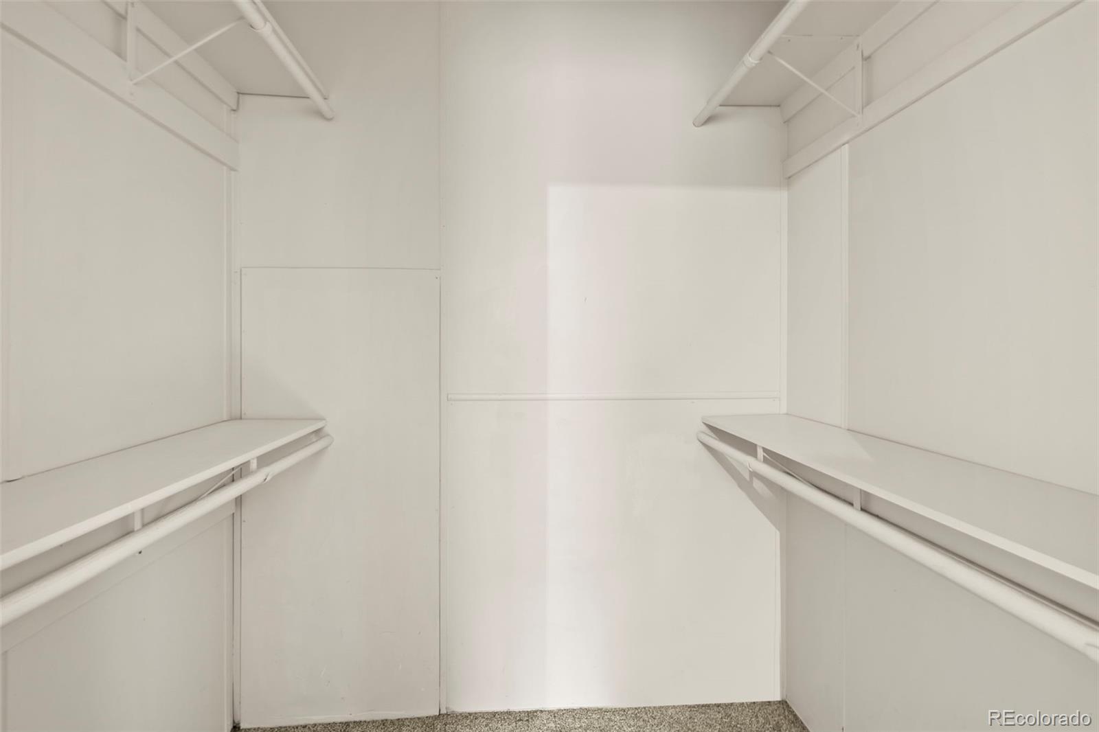 Empty walk-in closet with white shelving, hanging rods, and carpeted floor.