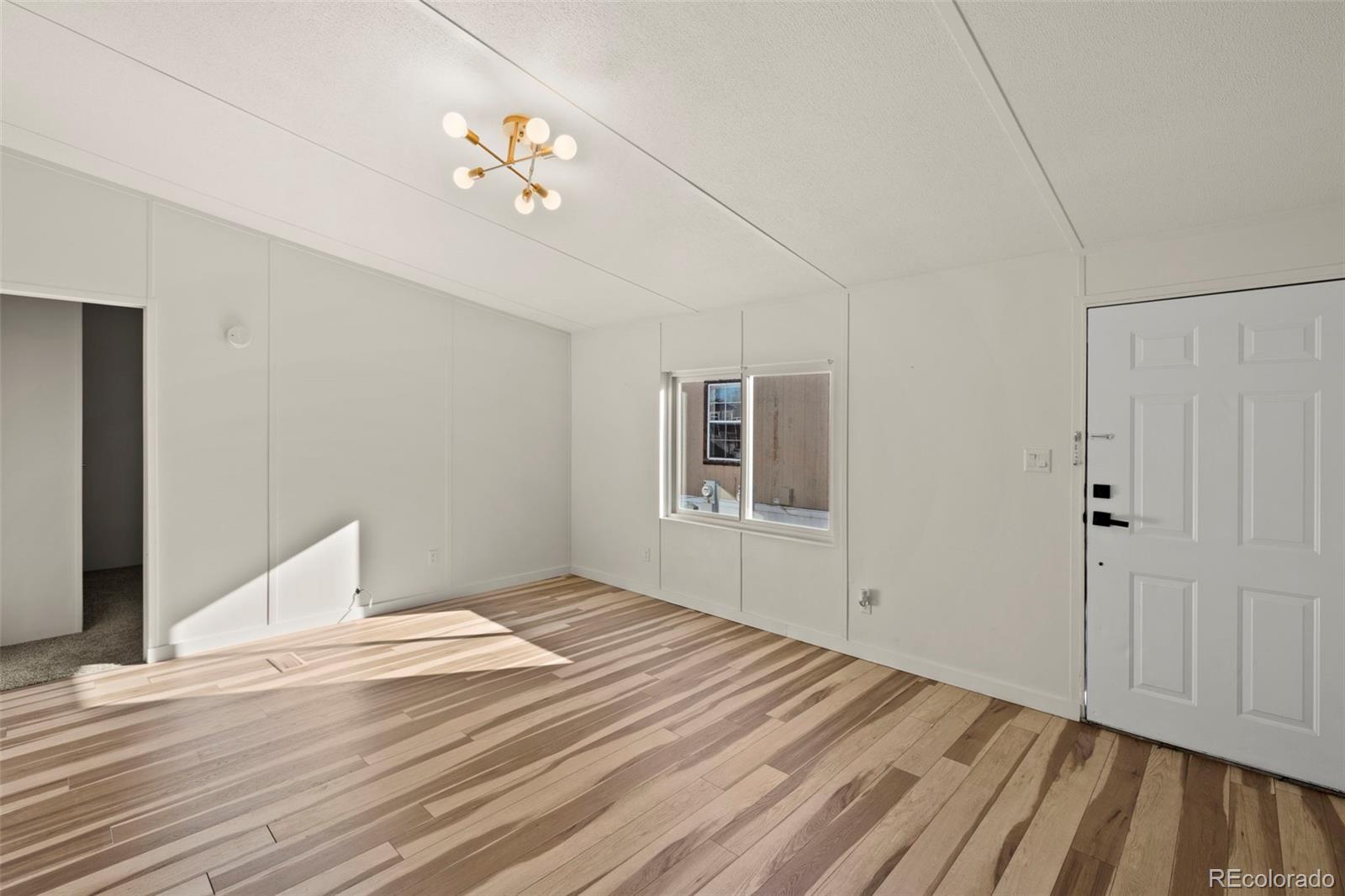 Empty room with varied-tone wood flooring, a front door, a window, and a brass ceiling light.
