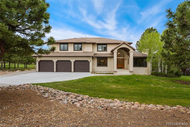 Two-story beige house with a three-car garage, arched entry, and broad landscaped front lawn.