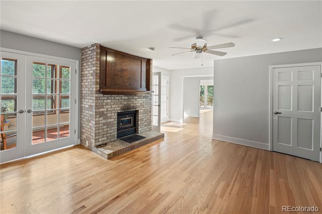 Empty living room with a brick fireplace, hardwood floors, and French doors opening to a deck.