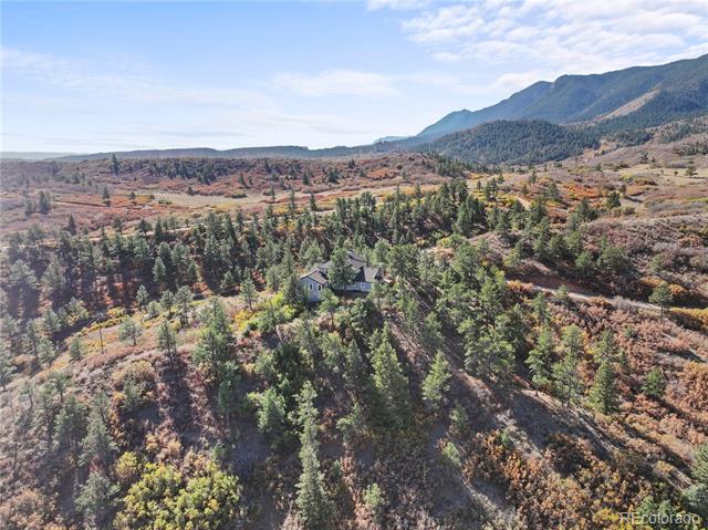 Aerial view of a secluded home among autumn trees, with a mountain range in the background.