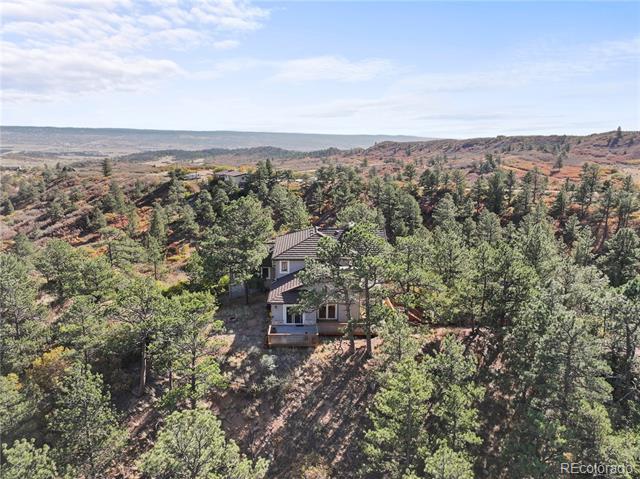 House nestled among trees on a wooded lot, with rolling hills visible in the distance.