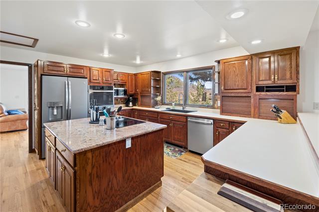 Kitchen with dark wood cabinets, a granite island, stainless steel appliances, and a window overlooking trees.