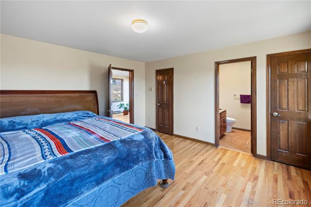 Bedroom with blue bedspread and hardwood floors, with an adjoining bathroom visible through open door.