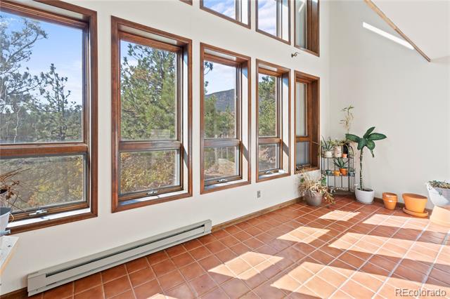 Sunroom with tall wood-framed windows, terracotta tile, potted plants, and a mountain view.
