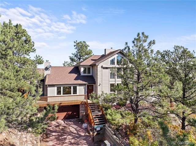 Multi-level house among pine trees, with a raised wooden deck and front stairs.
