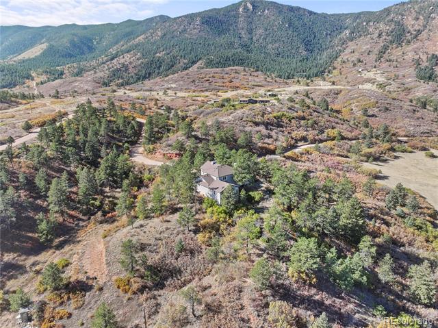 Aerial view of a house among trees and autumn-colored vegetation, with forested mountains beyond.