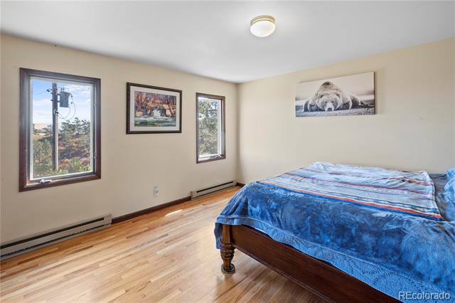 Bedroom with a blue-covered bed, light wood floors, and two windows.