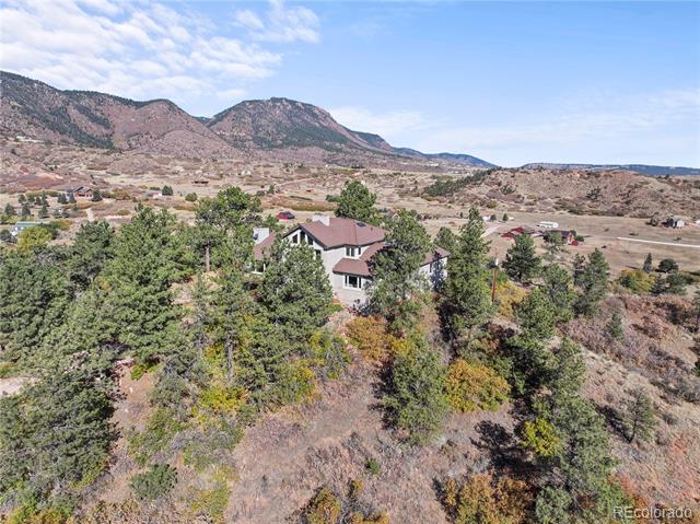 House among trees on a hilly lot, with a wide valley and rocky mountains beyond.