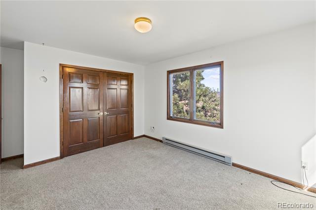 Empty carpeted room with dark wood double doors and a window overlooking trees.
