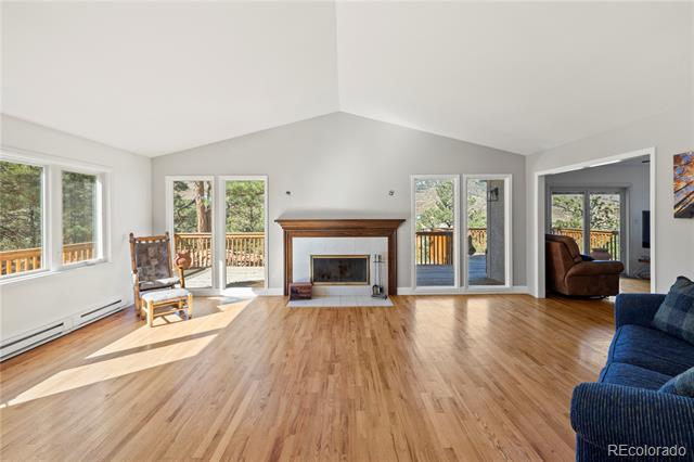 Bright living room with vaulted ceiling, wood floors, fireplace, and deck access.