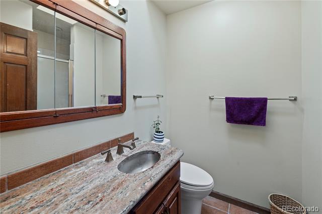 Bathroom with a wood vanity, speckled stone countertop, oval sink, and purple towel.