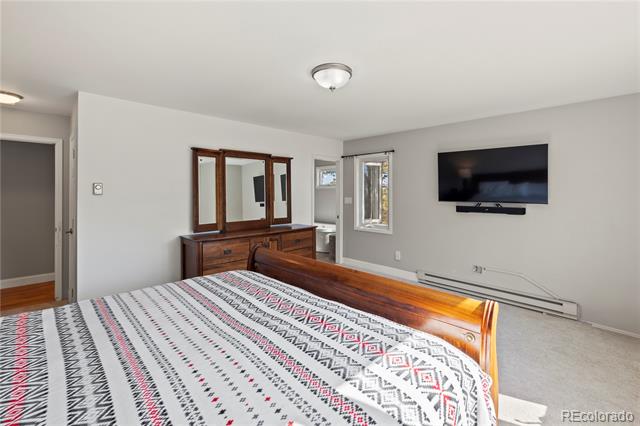 Bedroom with a geometric-patterned bedspread, wooden dresser and mirror, and wall-mounted television.