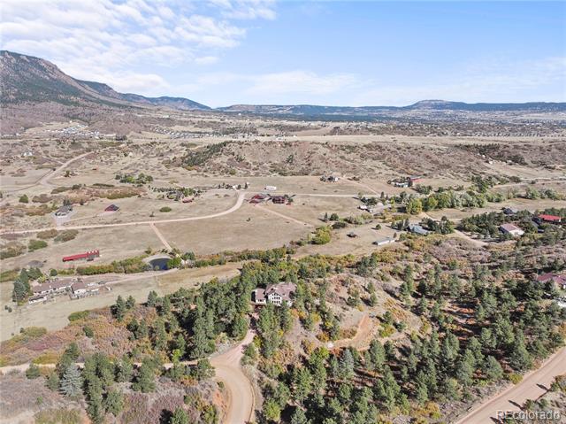 Aerial view of a home amid wooded acreage, open fields, and distant foothills.