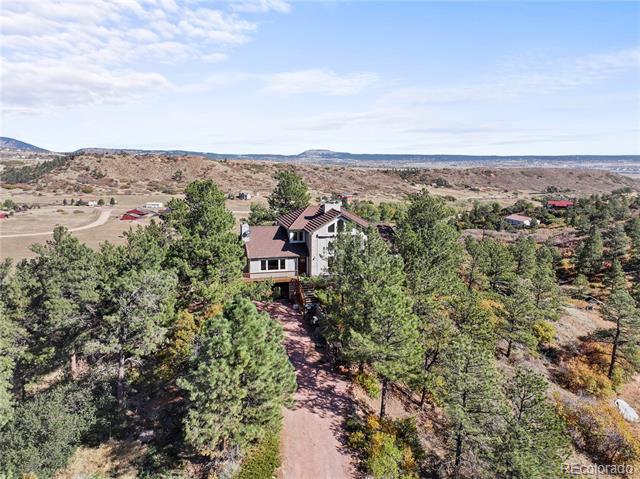 Aerial view of a two-story house tucked among pine trees, with rolling hills beyond.