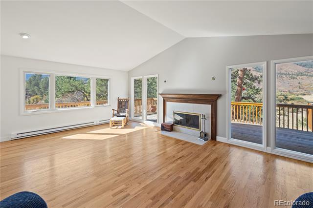 Living room with hardwood floors, a fireplace, and large windows overlooking a deck and mountains.