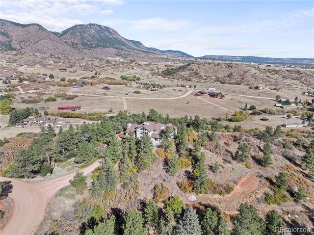 Aerial view of a wooded home and open acreage with mountains in the distance.