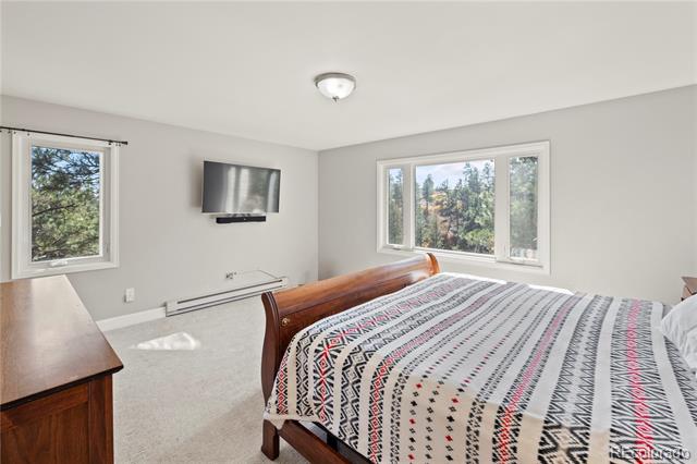 Bedroom with a wooden bed and patterned quilt, dresser, wall-mounted television, and windows overlooking trees.
