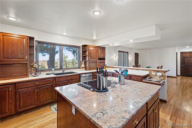 Kitchen with dark wood cabinets and a large granite island beneath a window overlooking trees.