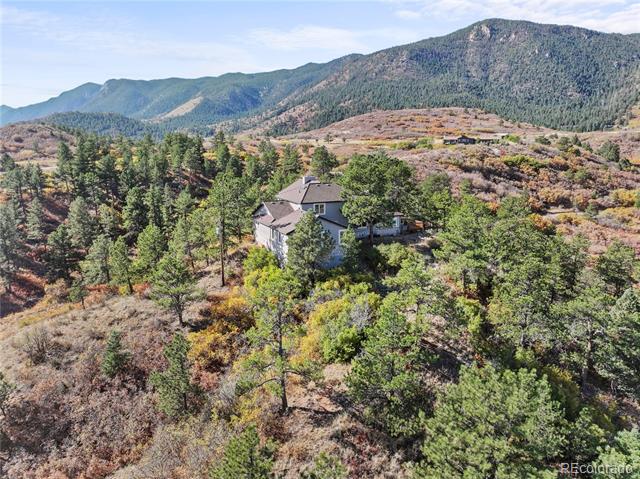 Aerial view of a house among trees and scrub, with forested mountains behind it.