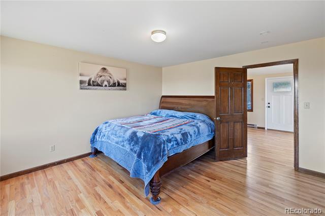 Bedroom with a blue patterned bedspread, hardwood floors, and an open dark wood door.