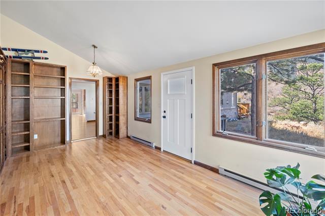 Mostly empty room with hardwood floors, built-in shelves, and large windows overlooking trees.