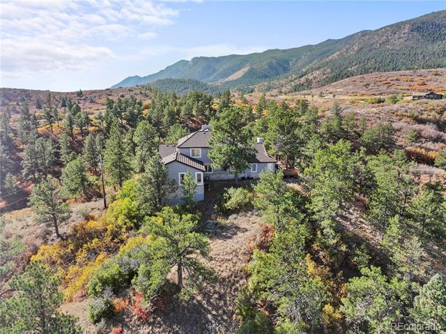 Mountain home surrounded by trees and autumn-colored shrubs, with forested hills behind it.