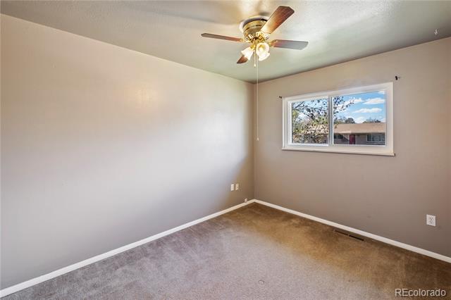 Empty bedroom with gray carpet, a ceiling fan, and a window overlooking trees.