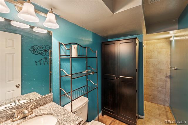 Bathroom with teal walls, a granite-look vanity, open shelving, dark cabinet, and tiled shower.