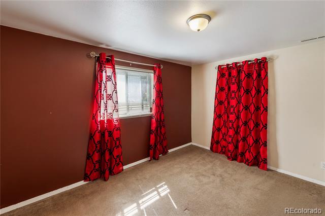Empty bedroom with beige carpet, a brown accent wall, and red patterned curtains.
