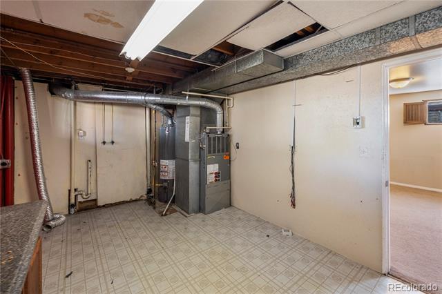 Basement utility room with a furnace, exposed ductwork, and patterned tile flooring.