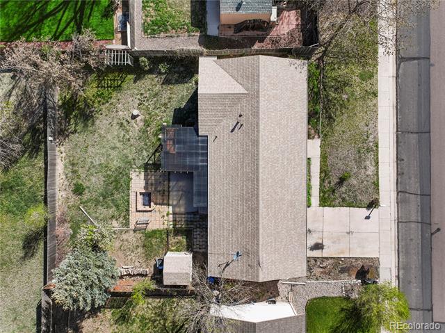 Aerial view of a home with a large roof, backyard patio, trees, and adjacent street.