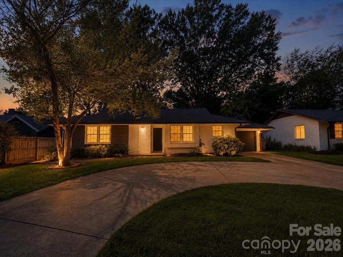 Single-story brick house at dusk with warmly lit windows and a curved driveway.