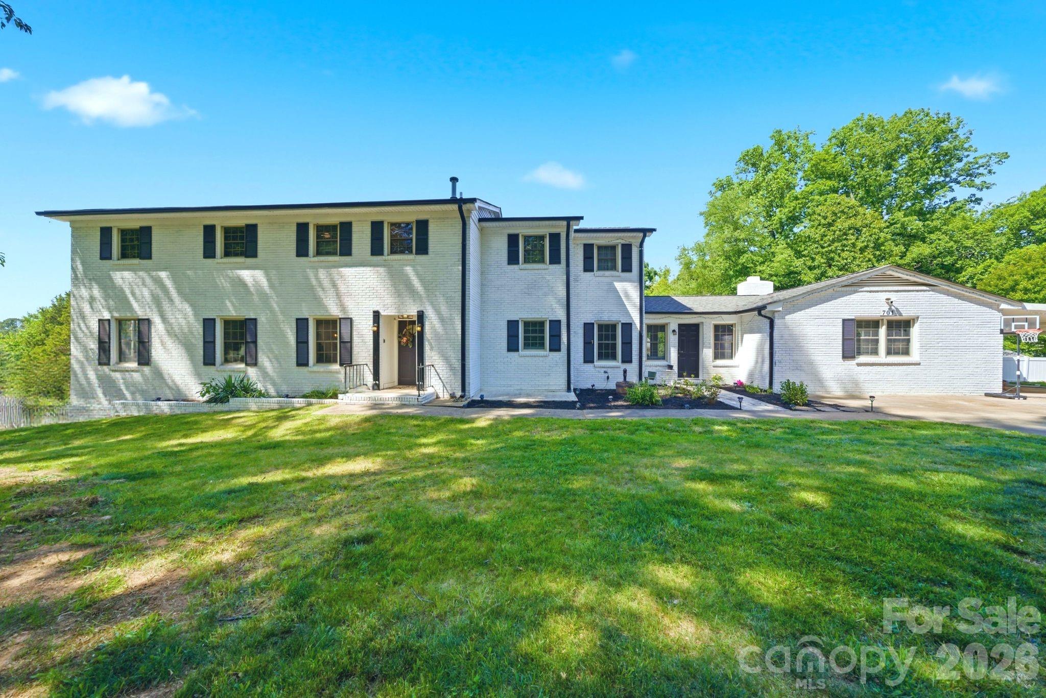 White brick home with dark shutters, a broad lawn, and a basketball hoop beside the driveway.