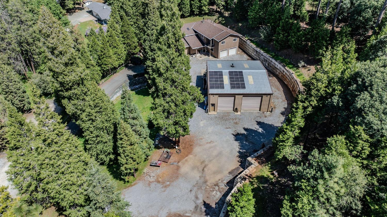 Aerial view of a wooded property with a two-story home and solar-panelled garage outbuilding.