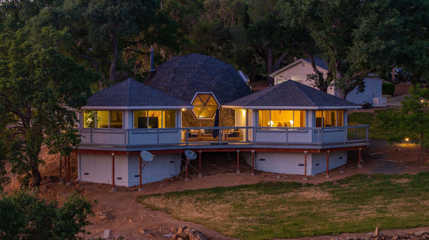 Elevated home at dusk with a wraparound deck and a distinctive illuminated hexagonal window.