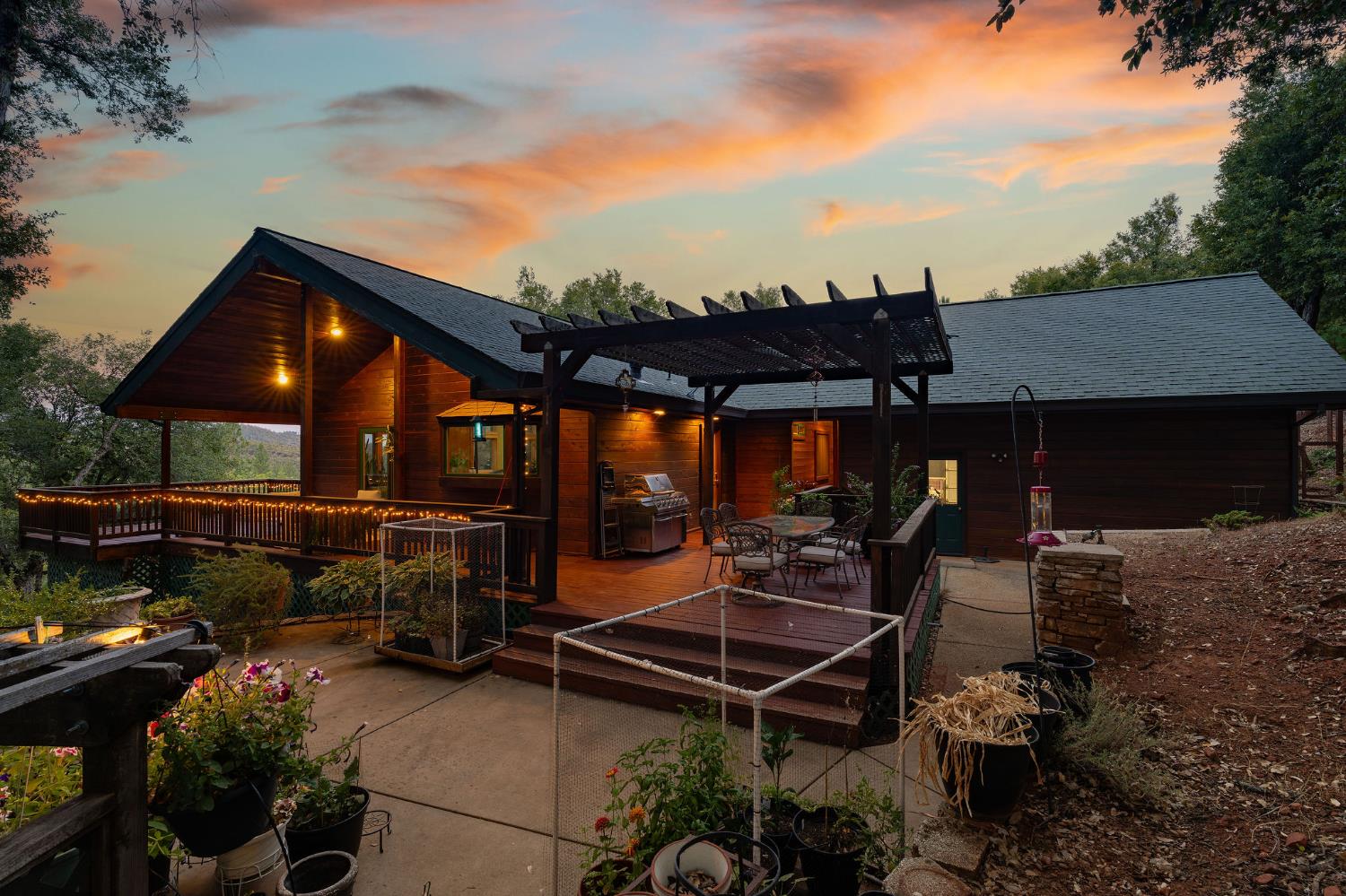Wood-sided home with a deck and pergola glowing beneath a colorful dusk sky.