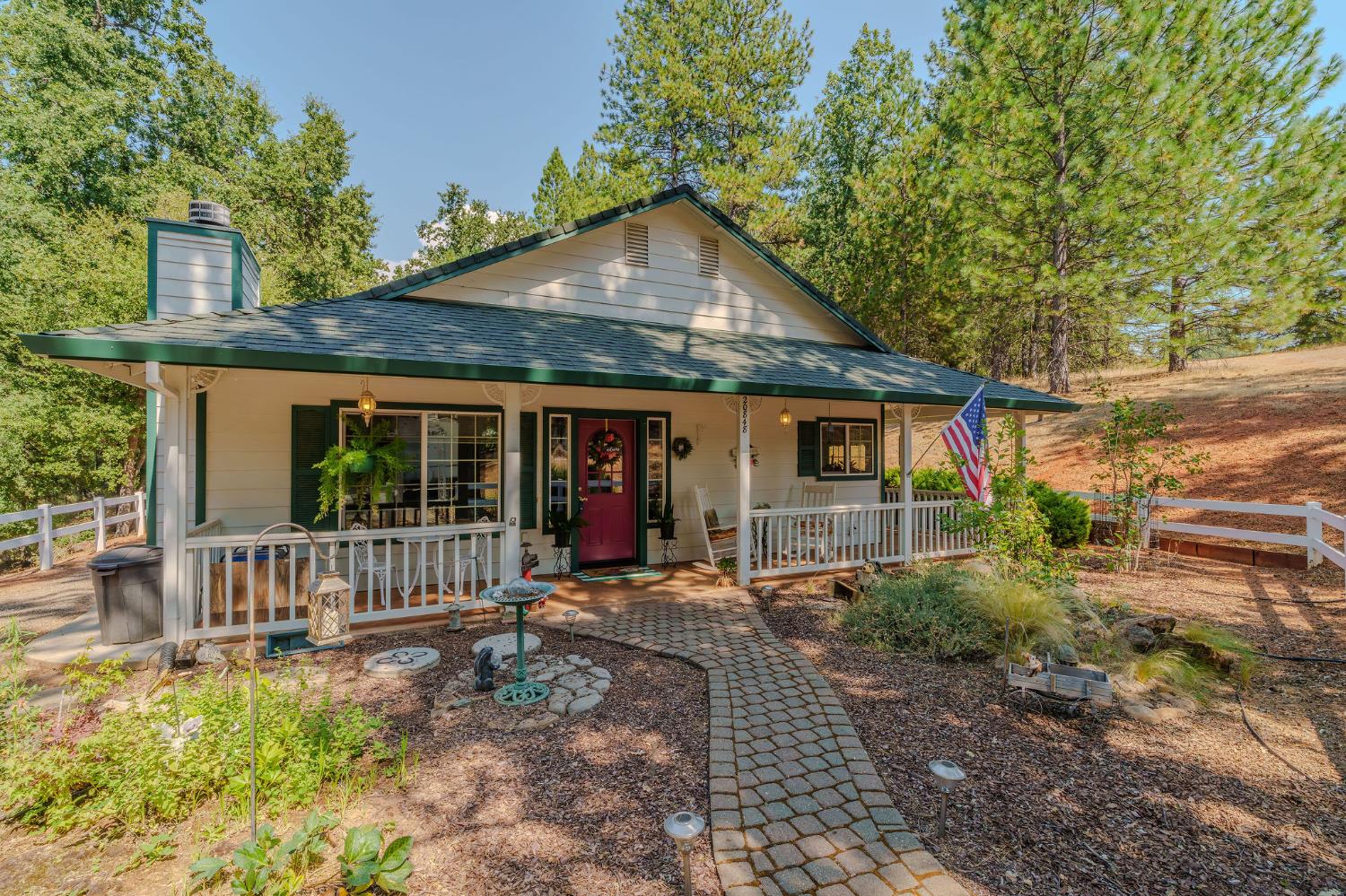 House with a covered porch, red front door, and stone walkway amid trees.