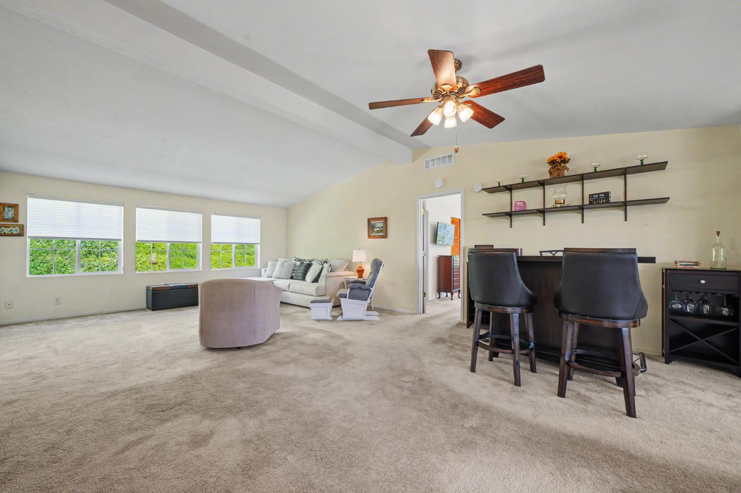 Open living and dining area with beige carpet, a white sofa, and a dark counter with tall chairs.