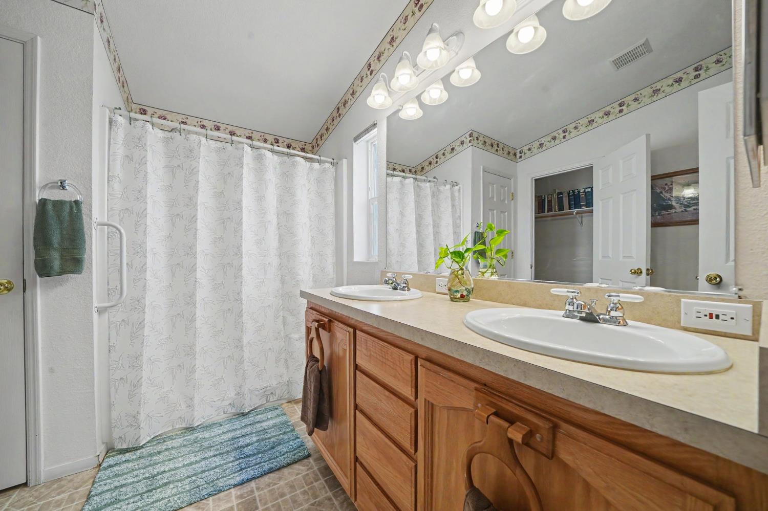 Bathroom with a wooden double vanity, large mirror, and floral ceiling trim.