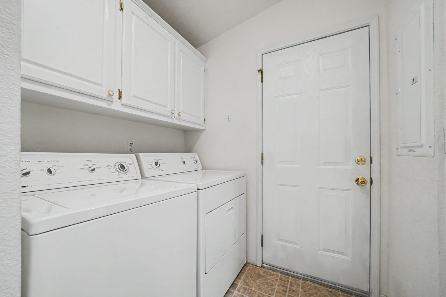 Laundry room with a top-loading washer, dryer, white upper cabinets, and a paneled door.